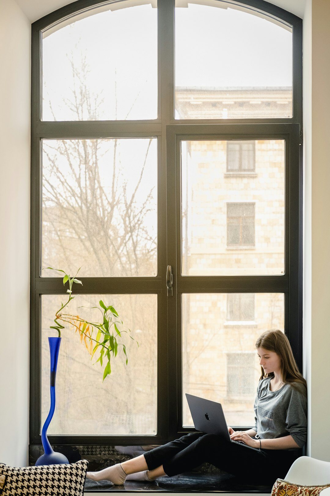 Woman working remotely from home with laptop near a window